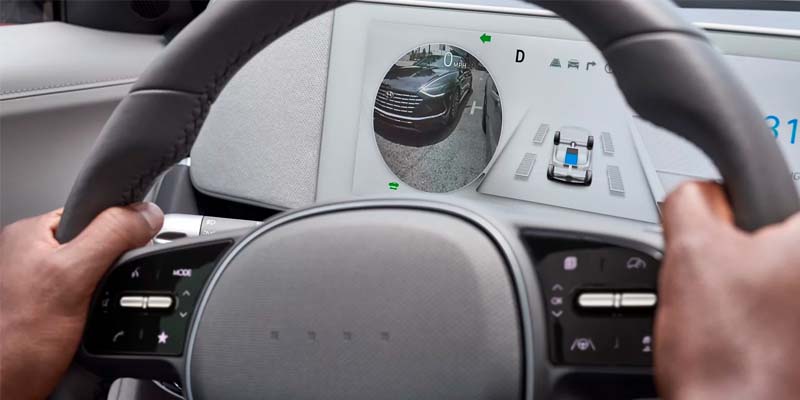 Driver’s view of a digital display showing a side camera feed and parking assist visuals.